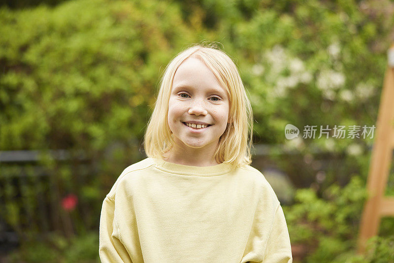 可爱的女孩对着镜头微笑的肖像，在花园里享受着平静的一天