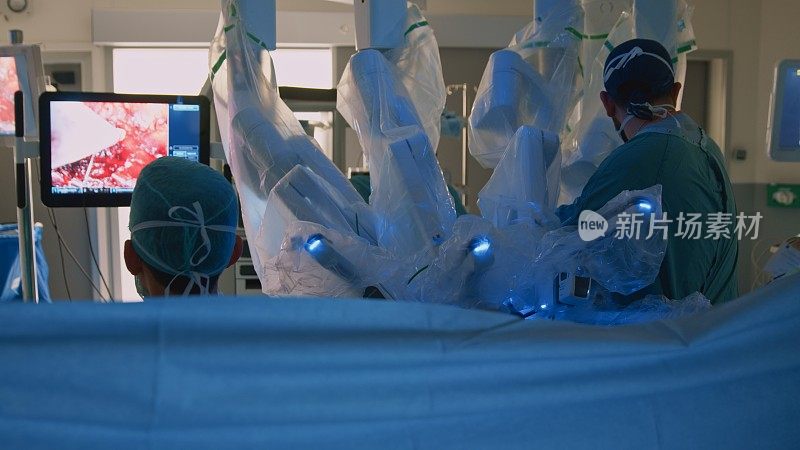 当外科医生进行手术时，护士看着显示器和医疗设备。