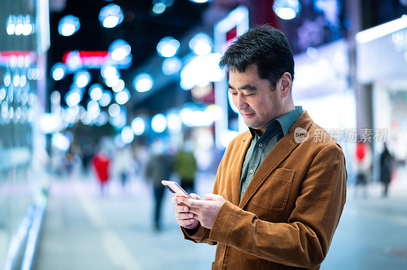 亚洲中年男子晚上在城市街道上使用智能手机