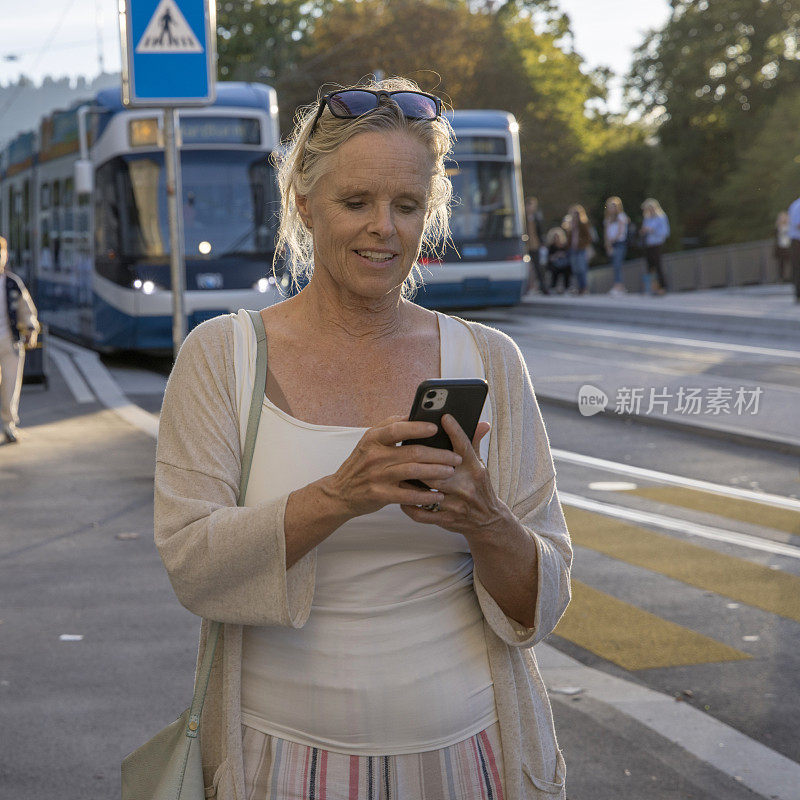 老妇人走在老城区的街道上，用着智能手机