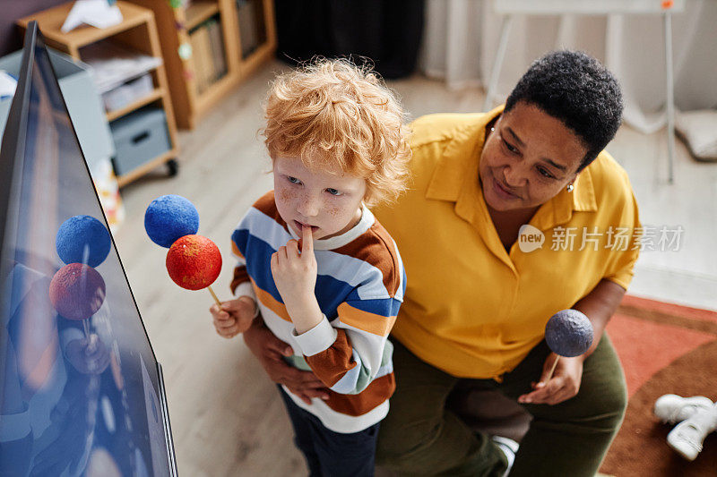 可爱的沉思男孩与地球和火星的模型看着互动板