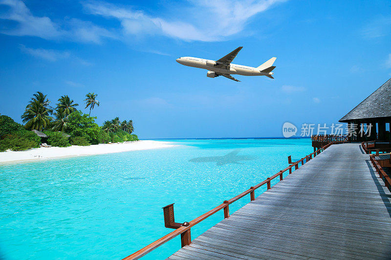一架白色飞机飞过热带海域，木制平台通往水上别墅