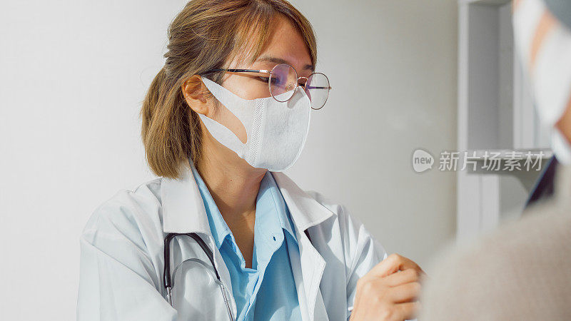 年轻的亚洲女医生戴着防护口罩，在健康诊所用平板电脑为癌症女性患者咨询医疗结果。医疗保健。