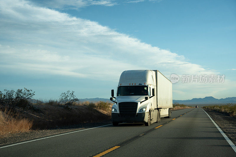 在美国西南部，一辆白色半卡车行驶在两车道高速公路上，天空中有美丽的云