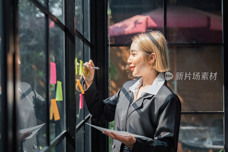 小公司的亚洲女企业家在分析制定商业战略时，在办公室的玻璃墙上贴了一张粘性便签