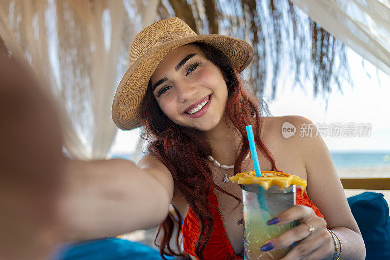 漂亮的年轻女孩穿着红色比基尼，拿着鸡尾酒杯在海滩上自拍。