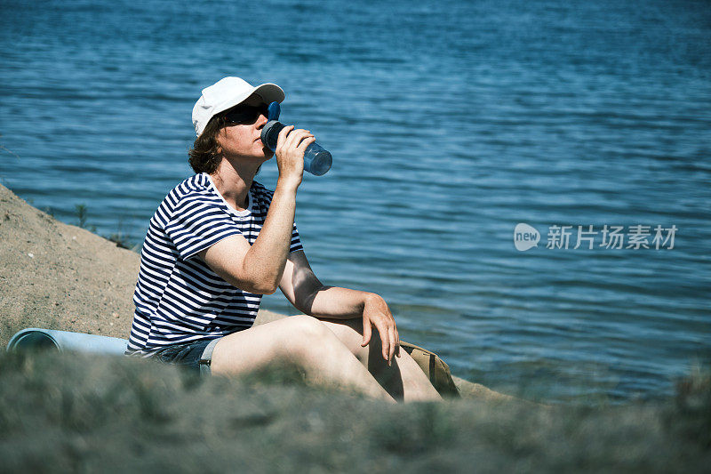 女游客坐在湖边沙滩上喝水