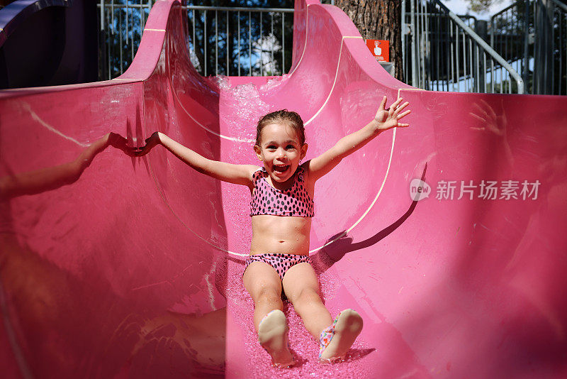 一个炎热的夏日，小女孩在室外游泳池里玩滑水