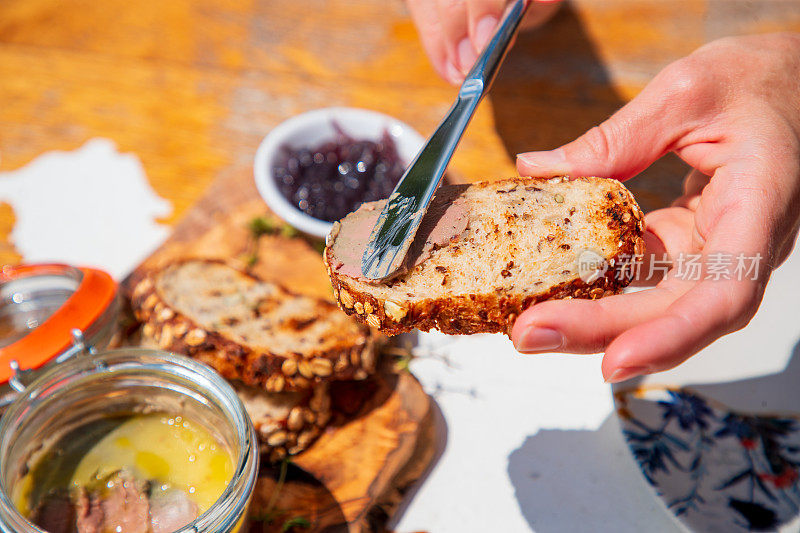 用餐刀在木桌上的全麦面包片上涂上鹅肉酱