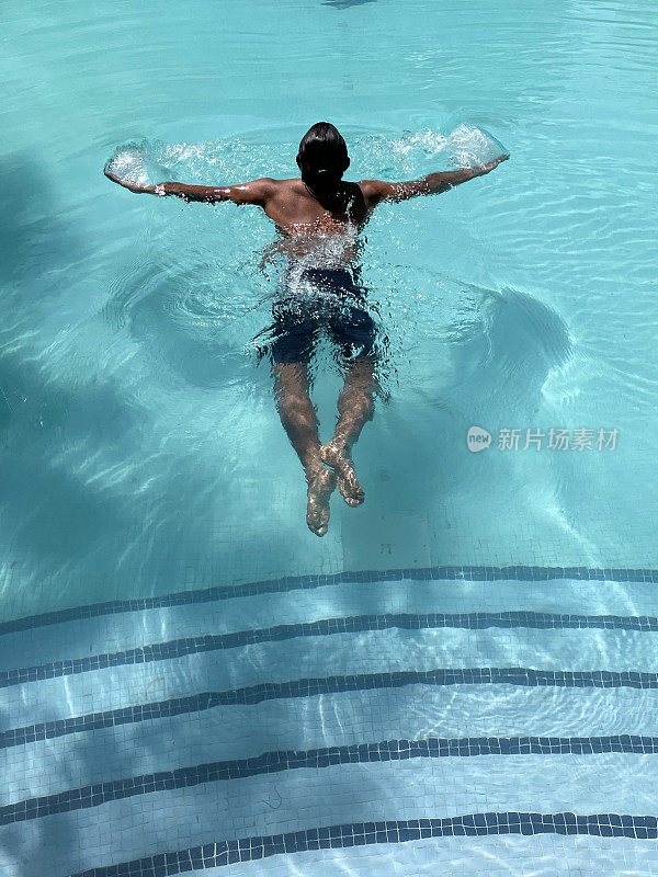 印度男子在清澈的水中做蛙泳的特写，室外，游泳池，碧蓝的马赛克瓷砖被波纹的水扭曲，游泳和飞溅，波涛汹涌的水面反射，抬高的视野