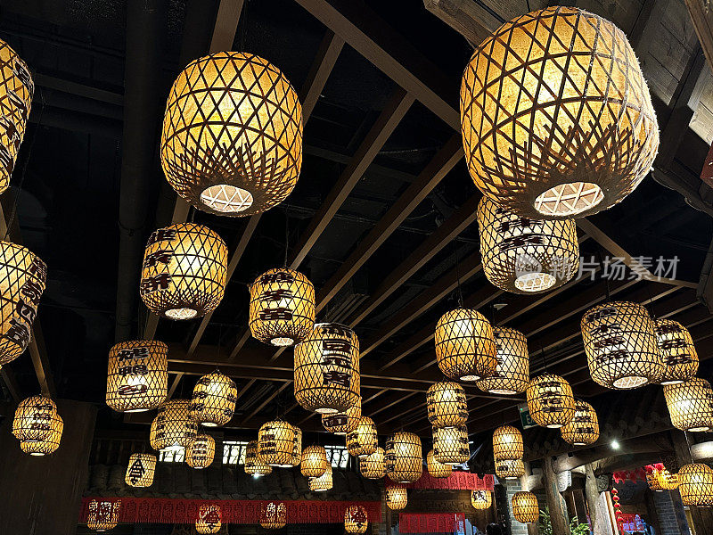 许多竹子和纸球灯悬挂在天花板上的特写图像，照亮发光的中国风格的灯笼室内照明，重点在前景，从下面看