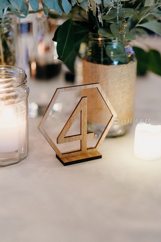 婚礼桌上的木制号码，玻璃罐里放着蜡烛，旁边是一个装满鲜花的花瓶