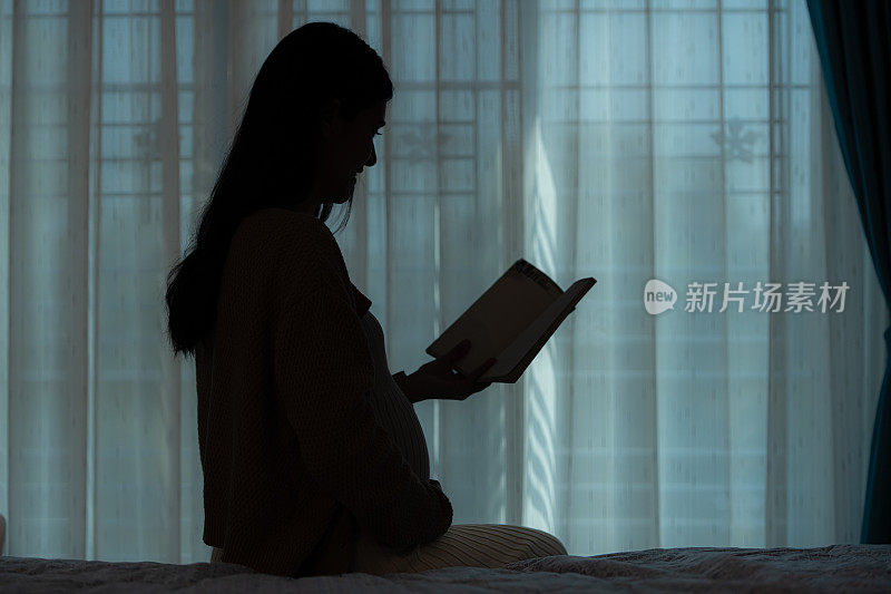 在剪影中，一位孕妇在家里的客厅里给她未出生的孩子读故事