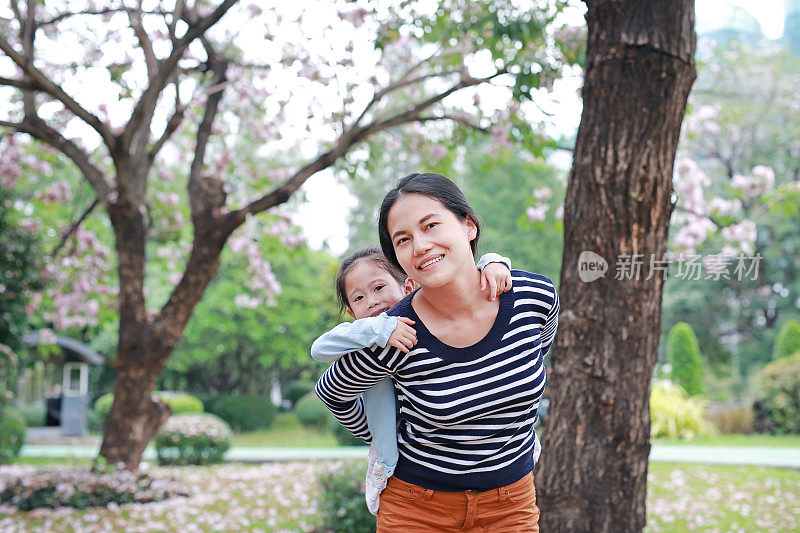 面带微笑的妈妈抱着她的小女孩在满是粉红色花朵的花园里。幸福美满的家庭。