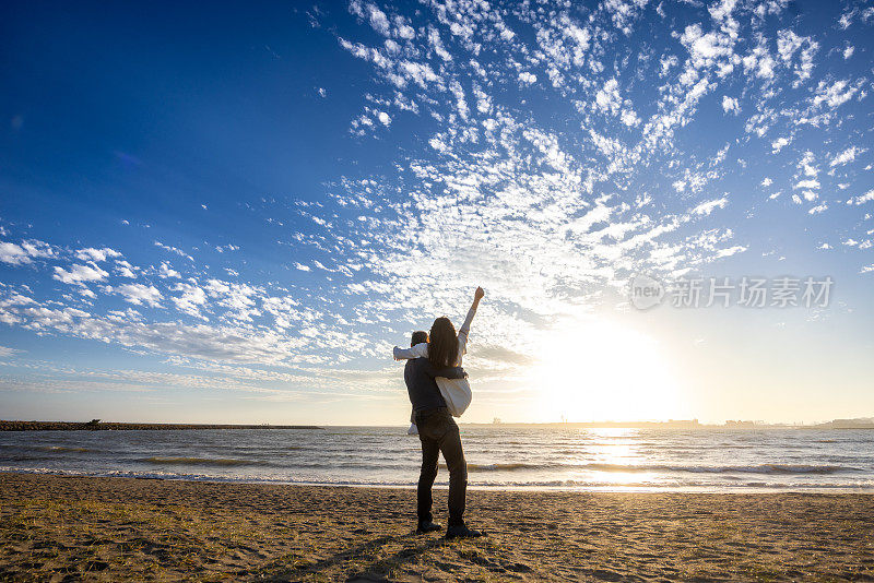 夕阳下沙滩上的一对情侣，在天空中举起手臂