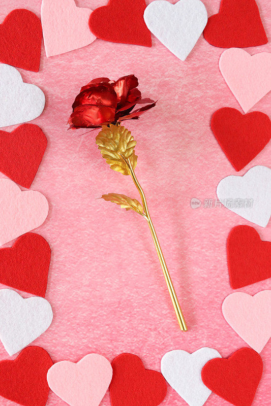 情人节设计海报框架的特写图像，由交替的红色，粉红色和白色的心形图案围绕金属，红色和金色的模型玫瑰，斑驳的粉红色背景，抬高的视图，情人节和浪漫的概念