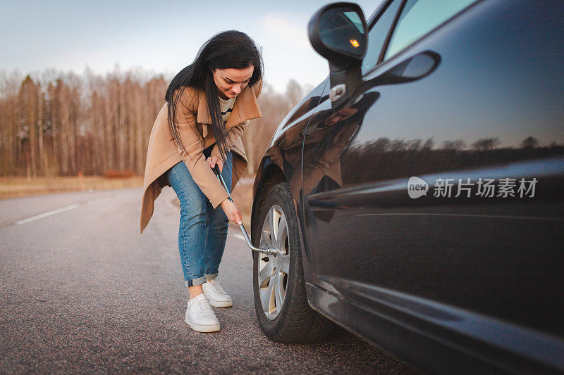 漂亮的年轻女子在路边给她的车换爆胎