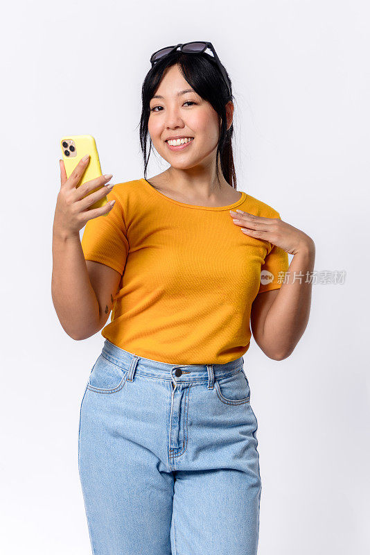 美丽的亚洲女人高兴地看着相机，同时接收手机上的重要信息。
