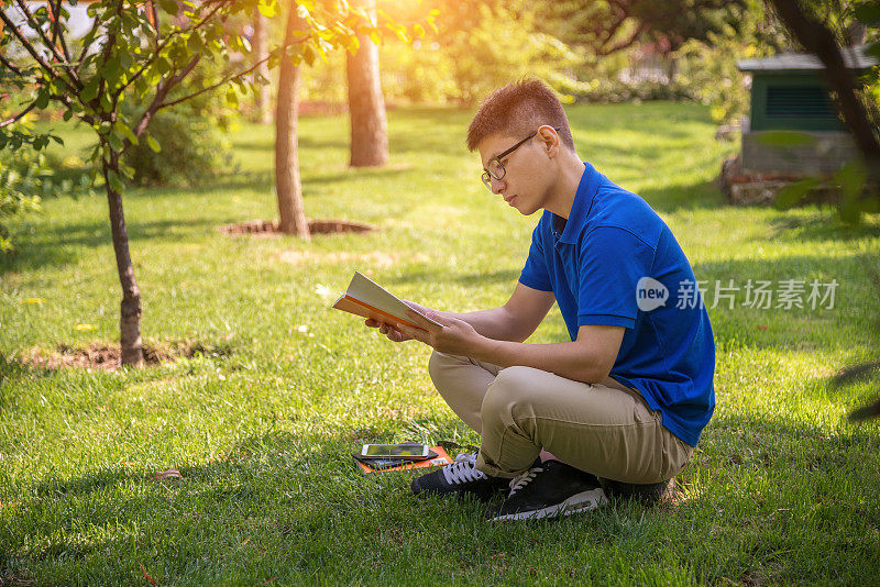 年轻英俊的亚洲男人坐在草坪上看书