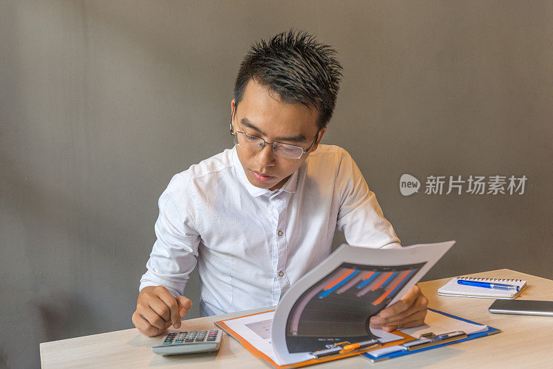 亚洲办公室职员穿白衬衫使用计算器检查销售报告