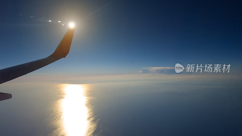 太阳在飞机的翼尖后，像镜子一样在海洋中