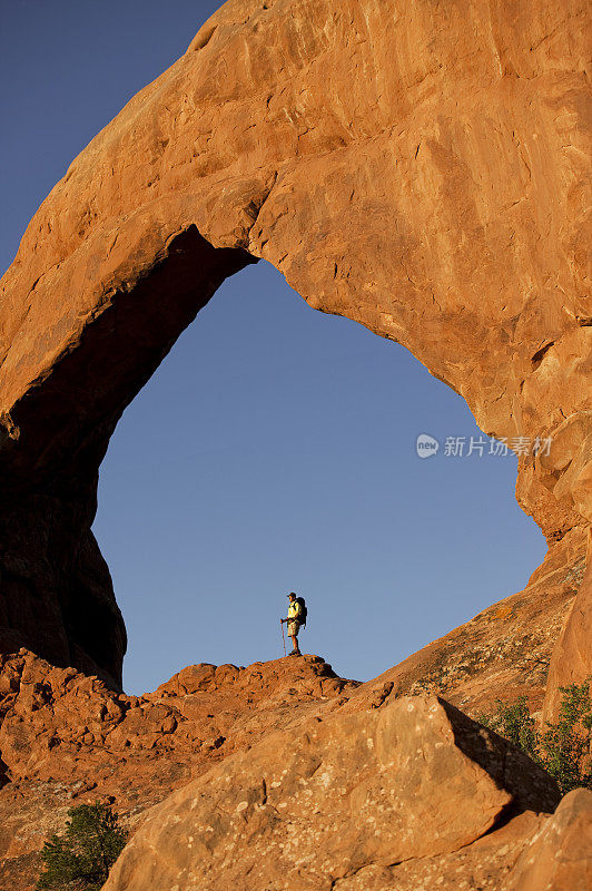 背包客站在犹他州巨大拱门下的岩石上