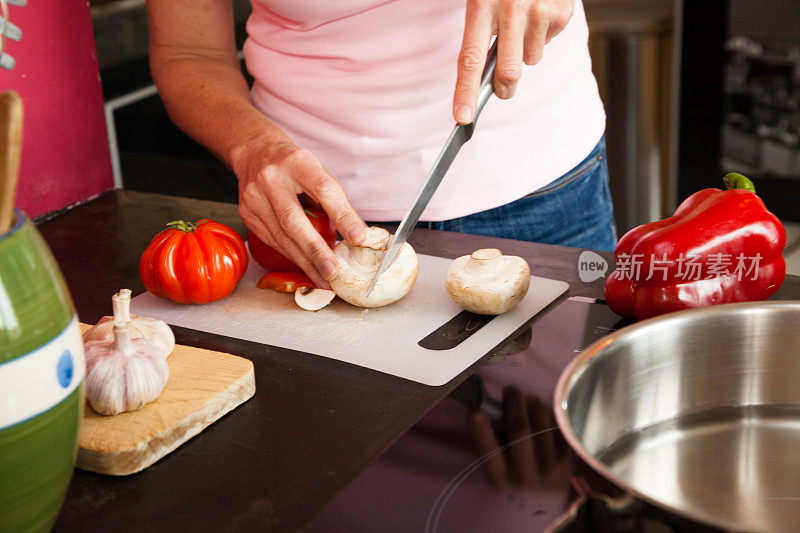 成熟的家庭主妇准备蔬菜，西红柿，蘑菇，胡椒，大蒜