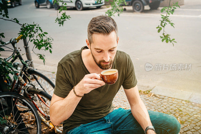 一个留着胡子的年轻人在柏林路边酒吧喝咖啡