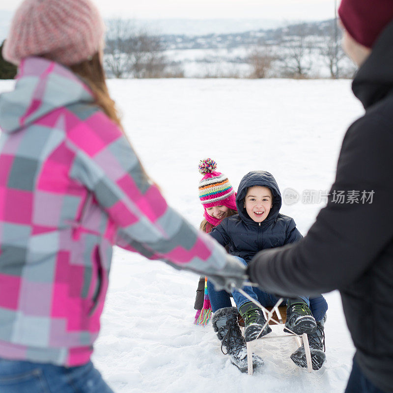 父母拉着雪橇穿越冬季景观