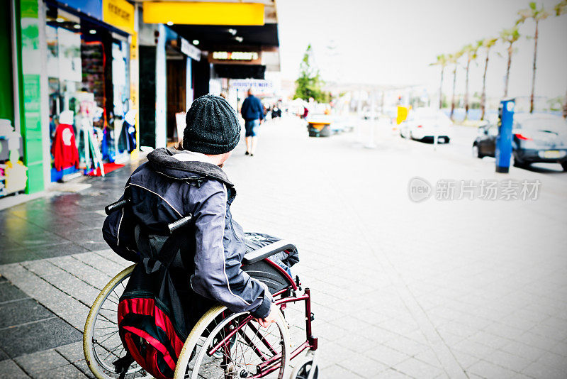 无家可归的年轻残疾人坐在轮椅上走在街上