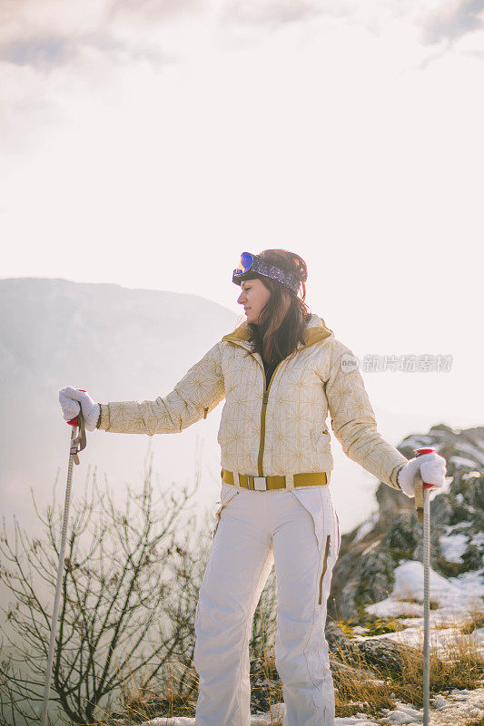 近景美丽的年轻女子在冬天的衣服站在一边，手拿木棍的背景雪山