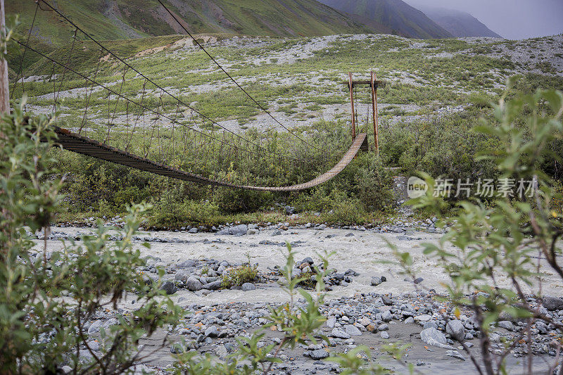 木制悬索桥横跨一条流淌的河流在阿尔