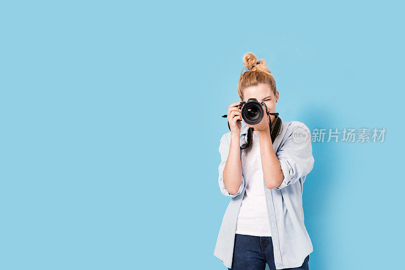 年轻的金发摄影师正在拍照。模型孤立的蓝色背景与复制空间