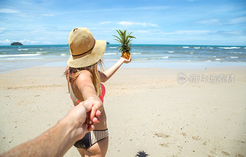 美丽的女孩穿着泳衣和菠萝走在海滩上，牵着男孩的手