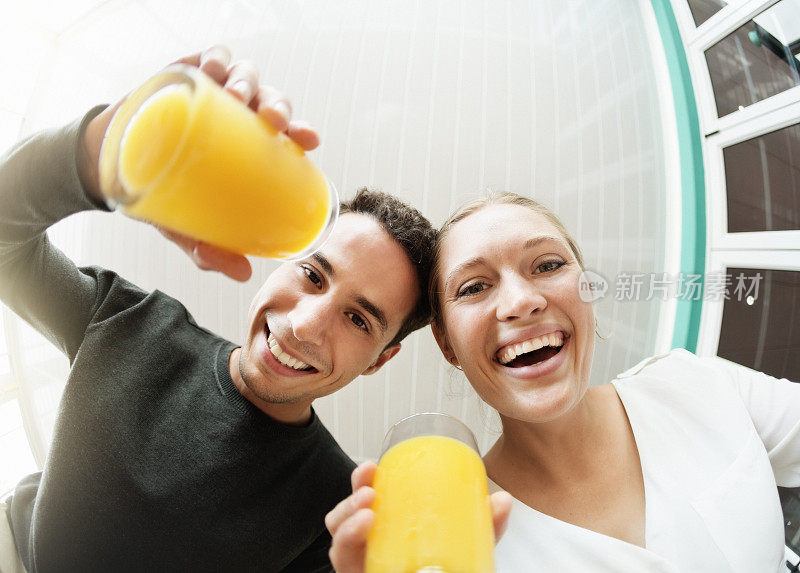 一对年轻夫妇被鱼眼的微笑扭曲，在橙汁中敬酒