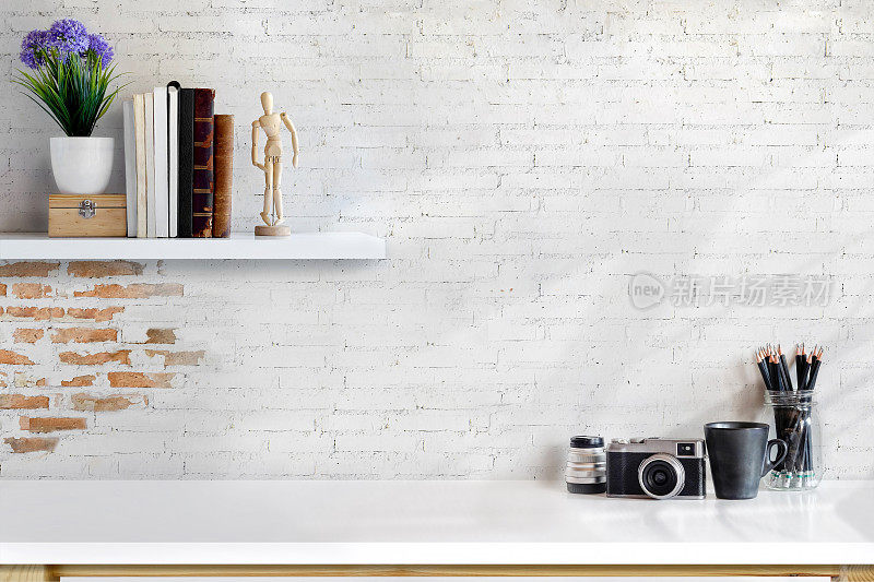 白色砖墙上的最小书桌和设计师工具的正面视图。复制空间的产品显示蒙太奇。