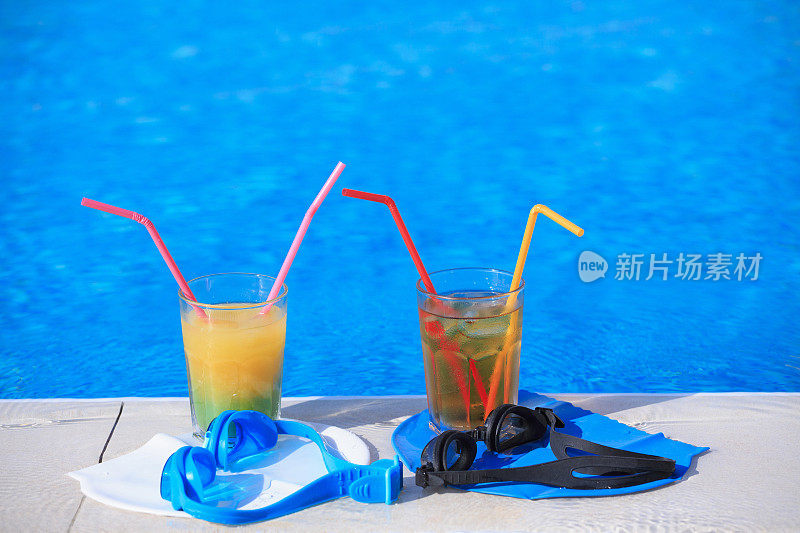 两杯配有彩色吸管的鸡尾酒和游泳池旁的游泳设备