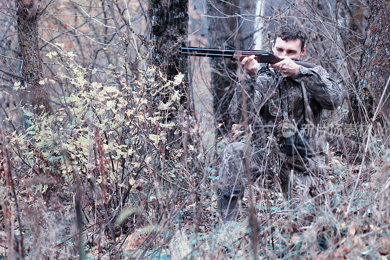 一名身穿迷彩服，手持猎枪的男子在森林里