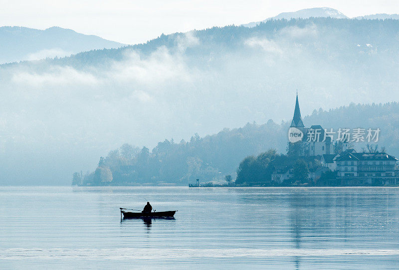 在雾蒙蒙的晨光中，孤独的渔夫坐在小船上，倒影在湖面上