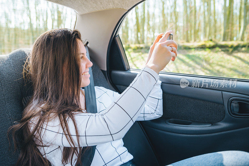 一个女人在汽车后座拍照。汽车旅行的概念