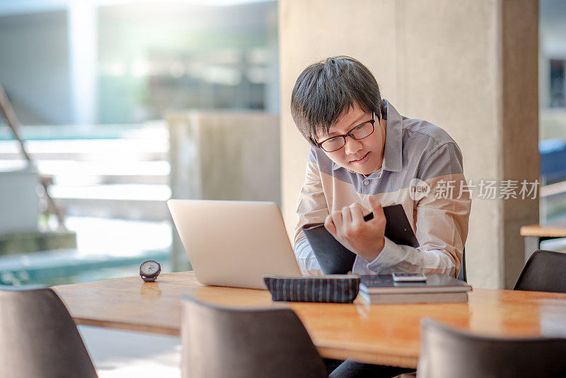 年轻的亚洲学生戴着眼镜，穿着休闲的风格，在大学大楼里看书和使用笔记本电脑。大学生活观念的教育研究与自学