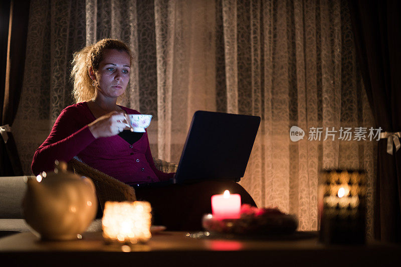 年轻女子在家里喝茶，用笔记本电脑。