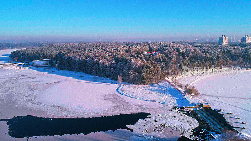 从空中俯瞰日落时冰冻的河流和森林的城市全景。