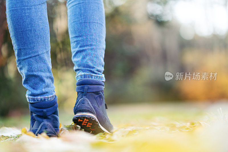 秋天，一名女子穿着登山靴，走在森林中的小径上。