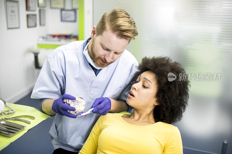 牙医示范如何正确地用牙刷和一套解剖牙齿模型给他的病人刷牙