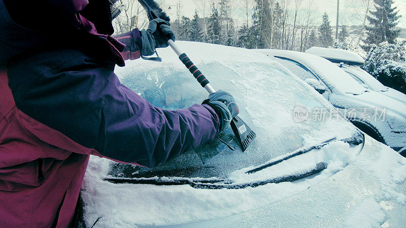 女司机刮着白雪覆盖的车窗