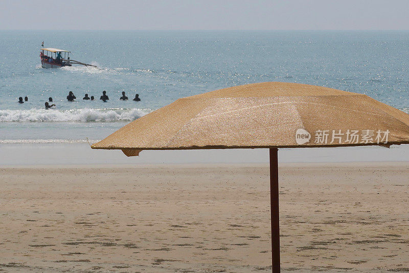 在印度果阿的帕洛伦海滩，棕色的海滩阳伞，度假者，游客和海滩游客在热带冬季度假，日光浴，在海里游泳
