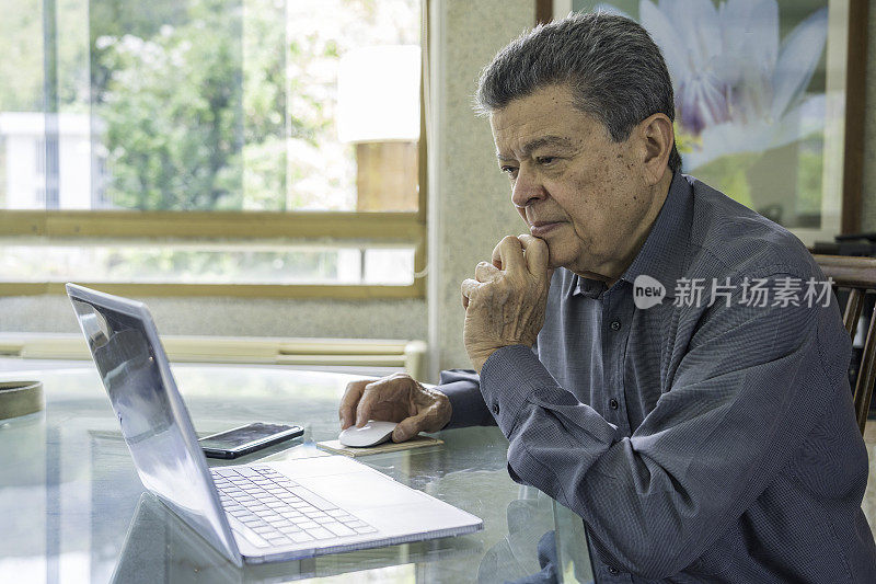 西班牙裔高级职员在家办公，使用笔记本电脑。家庭办公室的概念