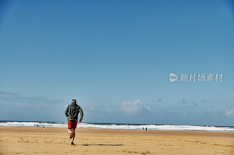 一个阳光明媚的秋日，康沃尔郡，沿着Perranporth海滩跑步的人。