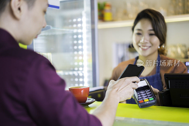 美丽的亚洲女服务员在café收到客户的手机无线支付。